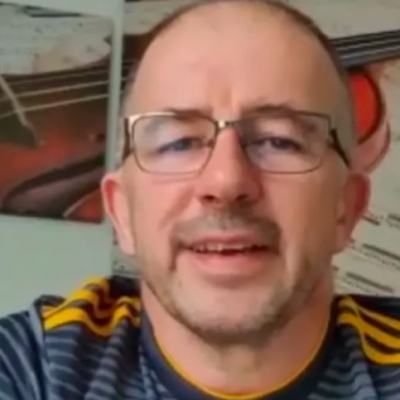 Close-up of a man wearing glasses speaking to camera indoors, with framed wall art behind him