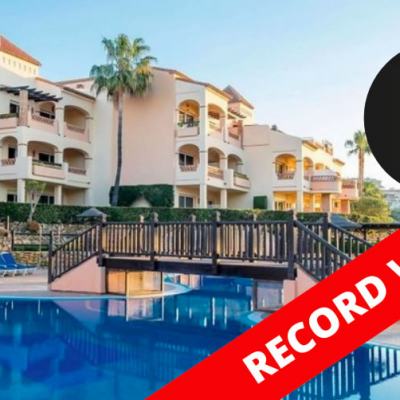 Outdoor swimming pool and bridge in front of a white holiday apartment complex with palm trees, overlaid with an M1 Legal logo and “RECORD WEEK” banner