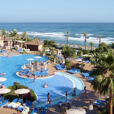 Oceanfront resort swimming pool with sun loungers, parasols and palm trees overlooking the sea in Spain
