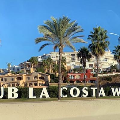 Club La Costa World entrance sign with palm trees and resort buildings on a hillside under a clear blue sky