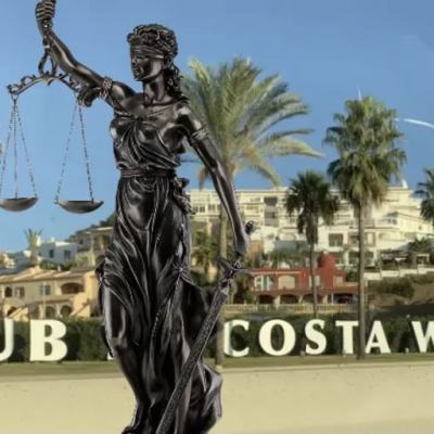 Statue of Lady Justice holding scales in front of a Club La Costa World sign with palm trees and resort buildings in the background