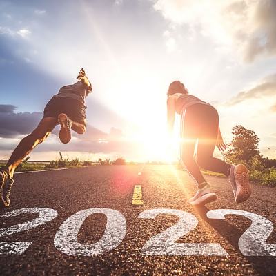Two runners sprinting down a road marked “2022” towards the sunrise under a cloudy sky