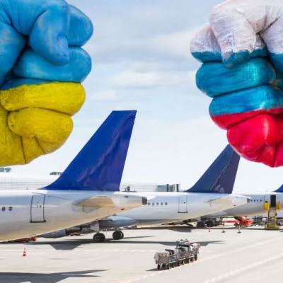 Painted fists in Ukraine and Russia flag colours facing each other above parked passenger aeroplanes on an airport tarmac