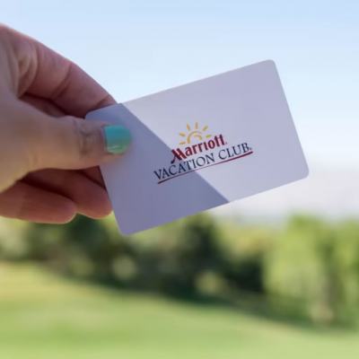 Hand holding a Marriott Vacation Club card against a blurred outdoor resort backdrop and blue sky