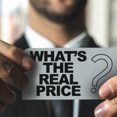 Person in a suit holding a card that reads “WHAT’S THE REAL PRICE” with a question mark icon