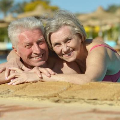 Smiling older couple relaxing at the edge of a resort swimming pool with sun loungers in the background