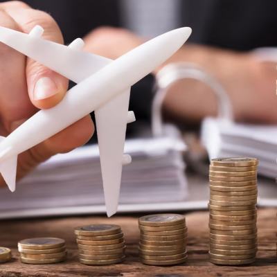 Hand holding a model aeroplane next to stacks of coins increasing in height, showing rising travel costs and fees