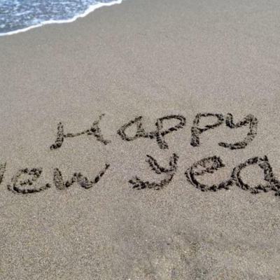 Happy New Year written in the sand on a beach beside the shoreline