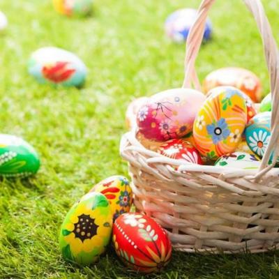 Basket of colourful painted Easter eggs on green grass with more eggs scattered around outdoors