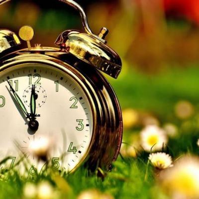 Vintage twin-bell alarm clock in grass with spring flowers, symbolising clocks spring forward for British Summer Time (BST) start in the UK