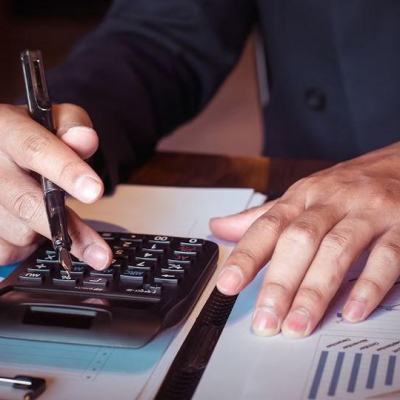 Close-up of a person using a calculator and pen over financial charts and paperwork, illustrating timeshare economics cost comparison calculations