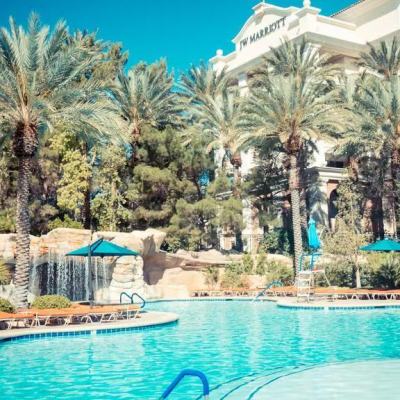 Outdoor hotel pool with sun loungers and palm trees, with a resort building in the background displaying “JW Marriott” signage