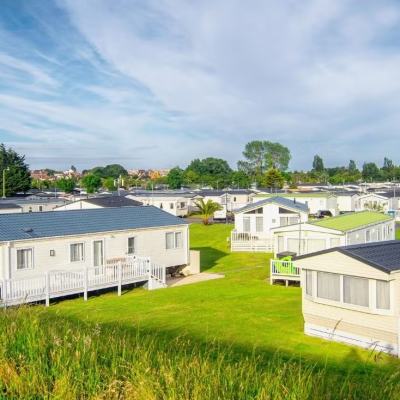Static caravan holiday park with rows of white lodges on green lawns under a cloudy blue sky