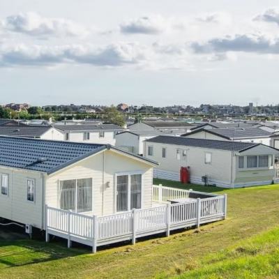 Row of static caravans on a UK holiday park, with white decking on a grassy slope under a cloudy sky